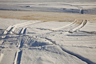 Snowmobile tracks across the tide mark where the edge of the ice fractures as water levels rise and fall with the tide
