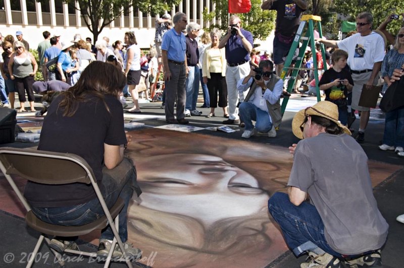 Local man, kneeling in shadows, shoots artist as she discusses her work.   Arraignment next Friday.