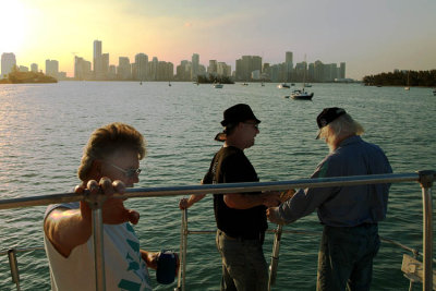 Terry Bocskey and Alan DeTomaso talking with Bob Zimmerman as he cooks on the grill with downtown Miami in the background