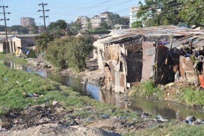 Slum dwellings with sewage draining into the stream in the foreground and high rises in the background