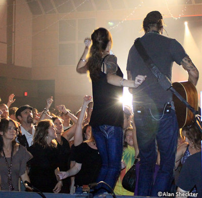 Michael Franti, with an invited audience member - performing a song from a platform out by the soundboard