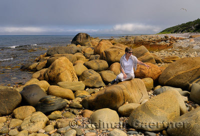 Traveler pointing at rust colored boulders on the shore of Martins Point Newfoundland