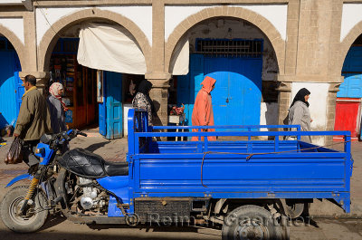 Morning shoppers in the Essaouira Medina with a blue motorcycle truck