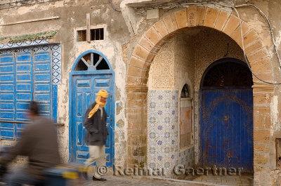 Passersby and blue doors in Essaouira Medina with ornate stonework and Zellige tilework