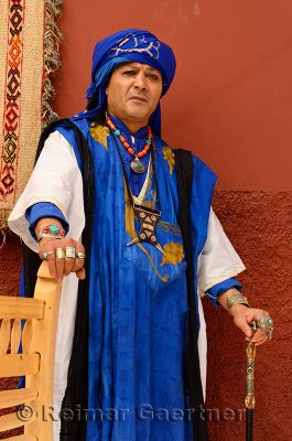 Traditional blue Berber Taureg man standing against a shaded red wall in Marrakech Morocco