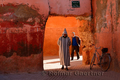 Two Moroccan men walking through an ochre arch in the souk of Marrakech