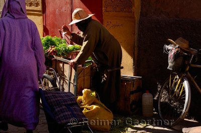 Woman farmer splashing water on her produce in the narrow alley of the souk in Marrakech