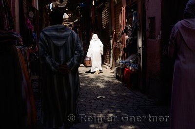 Old woman in white djellaba in a spotlight of sun in the narrow souk streets of Marrakech Morocco