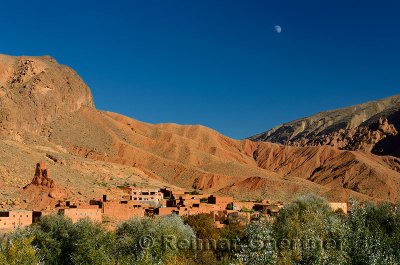 Moon in blue sky over red soil and rock formations in Dades Gorge Morocco