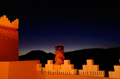 Adobe crenellations and chimney in gold light on rooftop of resort with indigo sunset in Tinerhir Morocco