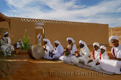 Group of Gnawa musicians in white turbans and jellabas sitting and playing music in Khemliya Morocco