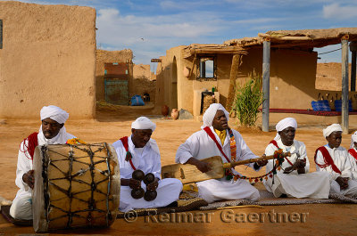 Khemliya Gnawa musicians in white turbans and jellabas playing while sitting in a desert village Morocco