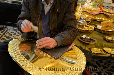 Worker with hammer and chisel engraving complex patterns on brass plate in Fes Morocco