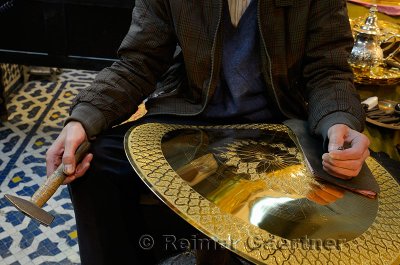 Worker with hammer and chisel showing work in progress engraving brass plate in Fes Morocco