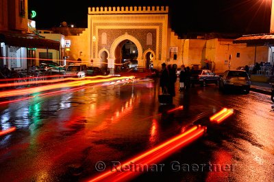Car taillights reflected on wet Place Boujeloud with Blue Gate Morocco at night