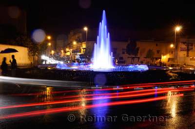 Couple under umbrella at night with wet traffic circle and blue fountain in Medina of Fes Morocco