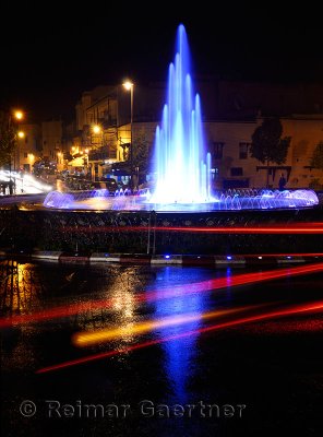 Car taillight reflections on wet Fes el Bali Medina traffic circle with blue fountain at night Morocco