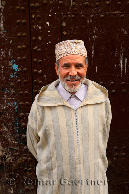 Smiling Moroccan man in djellaba and cap against an old door in el Bali Medina of Fes Morocco