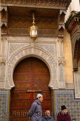 Men waiting at the ornate door of Sidi Ahmed Tijani Mosque with intricate stone carving in Fes Morocco