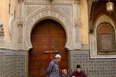Men at the ornate door of Sidi Ahmed Tijani Mosque with intricate stone carving and tilework in Fes Morocco