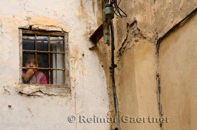 Pensive young girl staring out a small window in the el Bali Medina of Fes Morocco