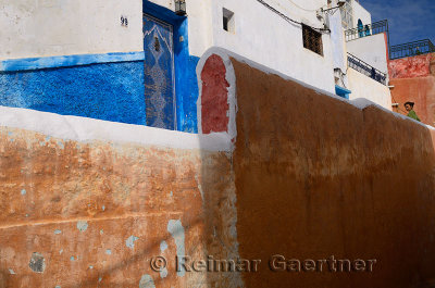 Young woman looking down from a red ochre wall in the blue city of Oudaia Kasbah Rabat Morocco