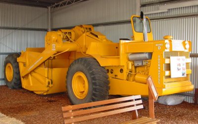 A late model, LeTourneau-Westinghouse, Model D Tournapull scraper. This machine is fitted with a 4 cylinder GM 2 stroke engine, a 5 speed crash gearbox, and has a big electric generator behind the engine, which produces electricity for the electric motors that power the steering, the lift motors on the bowl and apron, and the tailgate motor. These things are a handful to drive, and I know all about them, because I've actually got a licence to drive one! These machines need the main engine run at full RPM, or near it, to keep up the voltage to the electric motors. Otherwise, you run out of steering or power to load or empty the bowl. Early models were often known as widowmakers due to their tendency to kill operators who weren't properly trained on them. If you commenced a sharp turn and backed off the throttle - you couldn't straighten up, and they would sometimes roll over as a result. The early D's had multi-plate air disc brakes that would lock up all wheels at 40 mph, fully loaded. These brakes were incredible. However, when Westinghouse bought the LeTourneau Co in 1953, they commenced to put Westinghouse Air-operated drum brakes on the Model D's, saying that the material used in the original LeTourneau disc brakes was too deadly to continue using.