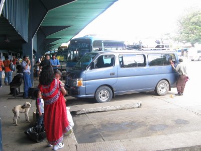 At the bus station- an indigenous woman in the colorful dress stands in the fore