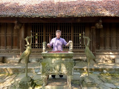 Me posing by a carved incense burner with storks on both sides of it at the entrance of But Thap Pagoda.