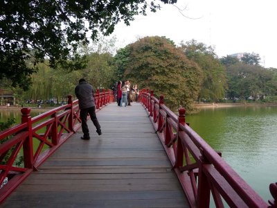 Strollers crossing over the Huc Bridge and the green water of Hoan Kiem Lake in Hanoi.