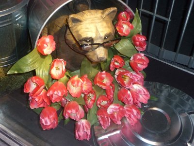 A raccoon wearing glasses in a knocked over trash can filled with roses.