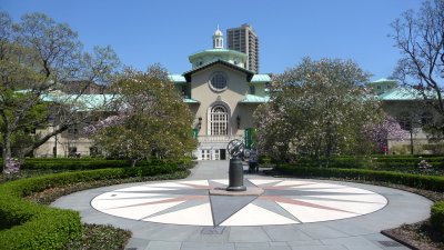 A large sun dial with the Magnolia Plaza and Visitors Center in the background.