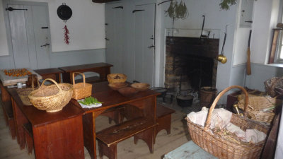 Interior of the small stone house with a fireplace, cooking pots, tables and baskets.