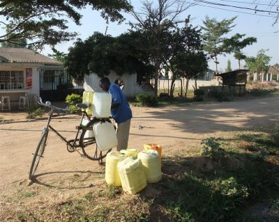 Man collecting his water supply from stream - he got them all on his bike!