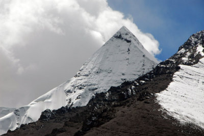 A sharp snow covered peak in front of clouds formed by the warm humid air of the Indian subcontinent