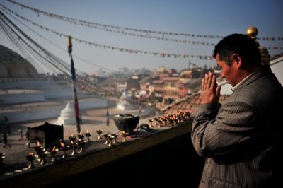 A man lit a candle at the Swayambhunath stupa, then put his palms together for prayer.