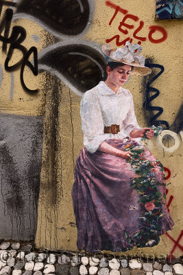 Frescoe painting of a woman in traditional dress with flowers amongst graffiti in an alley within the historic old town center o