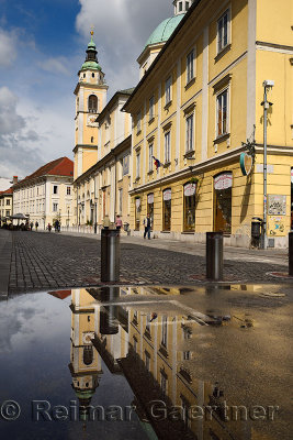 Clock and Bell tower of St. Nicholas Catholic church Ljubljana Cathedral reflected in a puddle on Cyril Methodius Square Ljublja