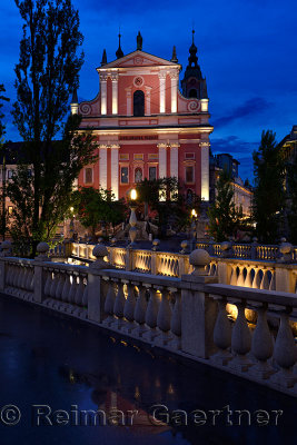 Pink facade of Franciscan Church of the Annunciation at dusk with concrete balustrades of Triple Bridge designed by Joze Plecnik