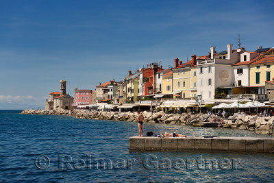 Young couple fishing reading sunbathing on dock at Piran Slovenia on the Adriatic Sea coast with Church of St Clement at Punta L