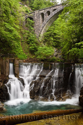 Single arch stone bridge for Bohinj railway over the Radovna river valley at Vintgar Gorge with log and waterfalls at Dam sluice