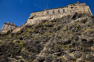 Volcanic plug cliff face of Castle Rock with red Valerian and Great Hall of the Royal Palace of Edinburgh Castle with blue sky i