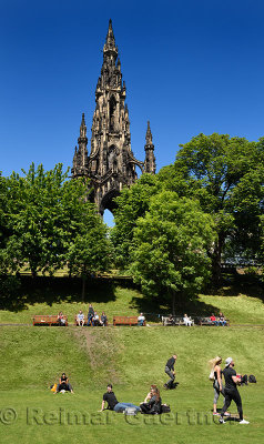 People and tourists in Princes Street Gardens park under the Scott Monument in Edinburgh Scotland UK with blue sky
