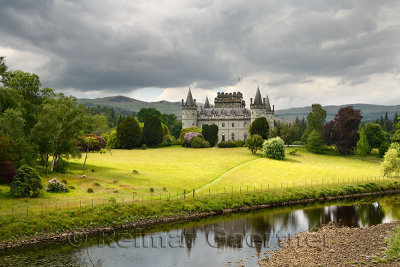 Inveraray Castle reflected in the River Aray with dark clouds and golden grass in the Scottish Highlands Scotland UK