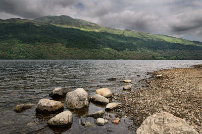 Rocky shore of Loch Lommond freshwater lake dividing lowlands from Scottish Highlands and Ben Lamond mountain Scotland UK