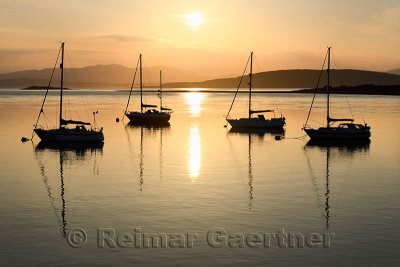 Setting sun over Ardmucknish Bay at North Connel and Oban Airport with sailboats in silhouette