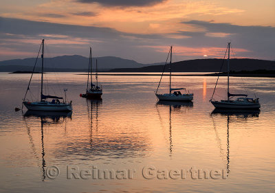 Red sky and clouds at sunset reflecting on the water of Ardmucknish Bay at North Connel with sailboats and Lismore island in sil