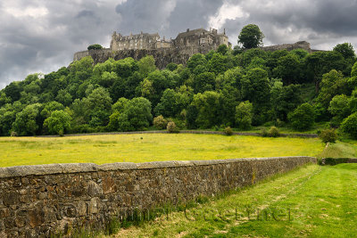 Stirling Castle on the cliff at Castle Hill in Stirling Scotland with stone wall of sheep pasture with dark clouds