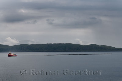 Tug boat pulling six fish farm cages along the Firth of Lorn between Isle of Mull and west coast Highlands of Scotland UK
