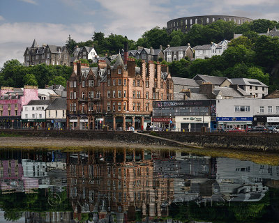 Historic buildings and McCaigs Tower on Battery Hill overlooking Oban harbour with water reflections in Oban Bay Scotland UK